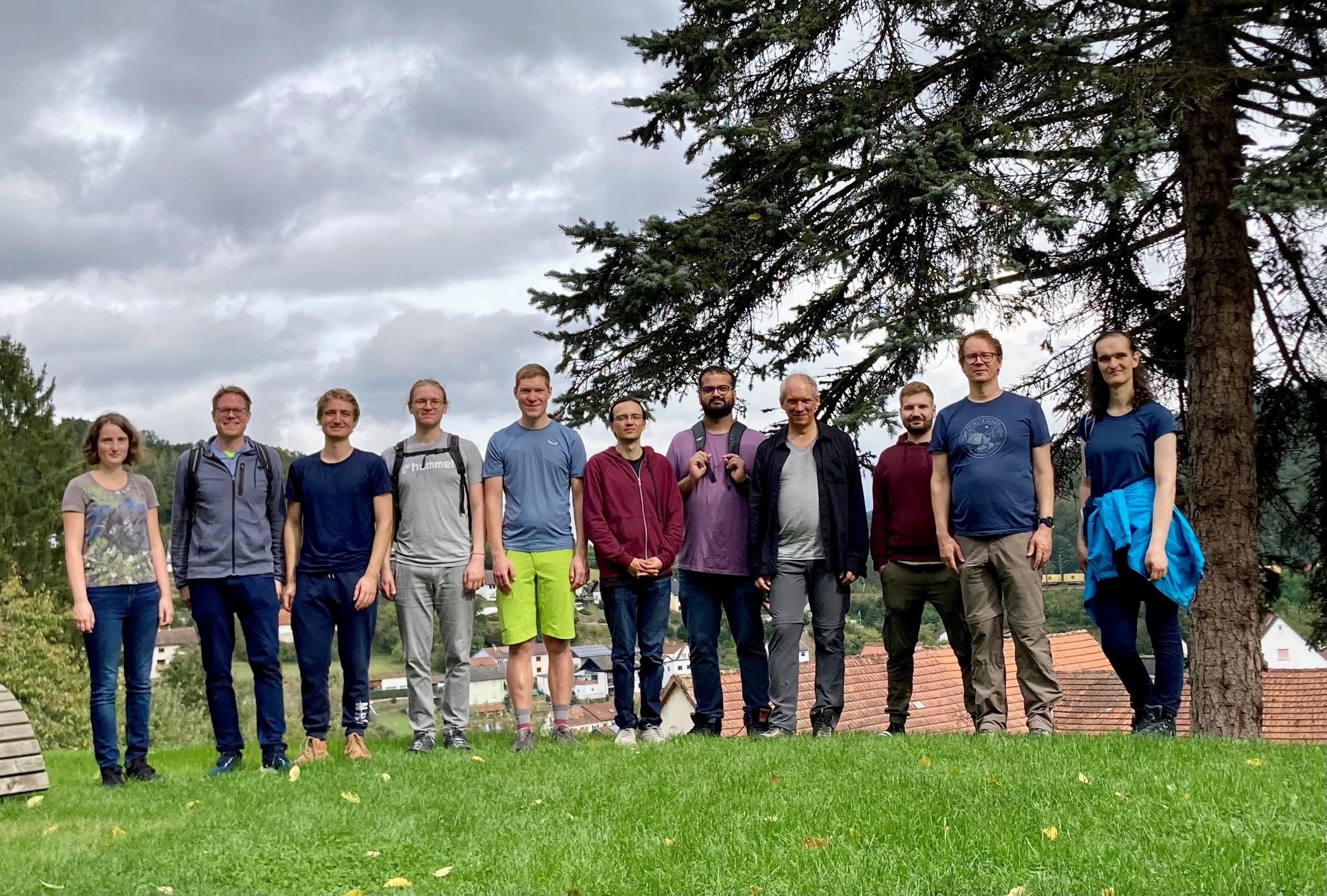Gruppenbild vor bewölktem Himmel und einer Fichte